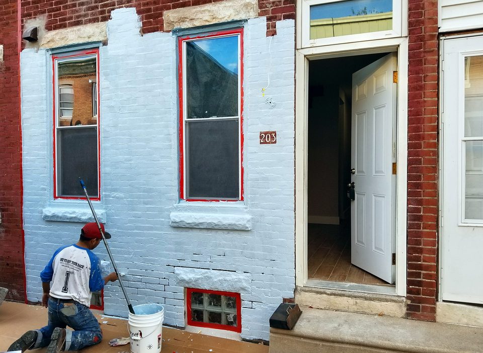 Painter coating a brick rowhouse facade, 2017