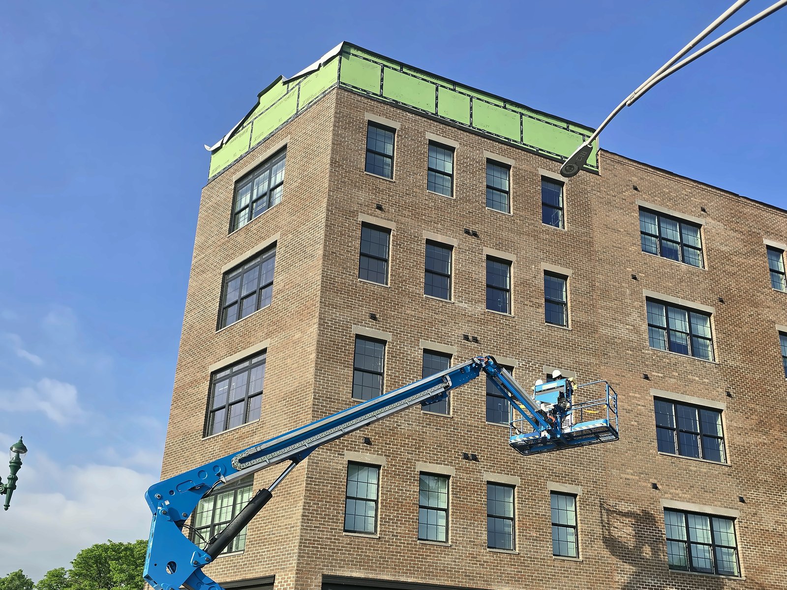 Boom lift raised to the top band of a five-story brick building in downtown Schenectady during EIFS panel installation