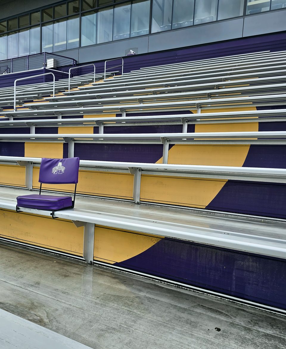 Before: chalked, faded purple on the bleacher risers, July 2026
