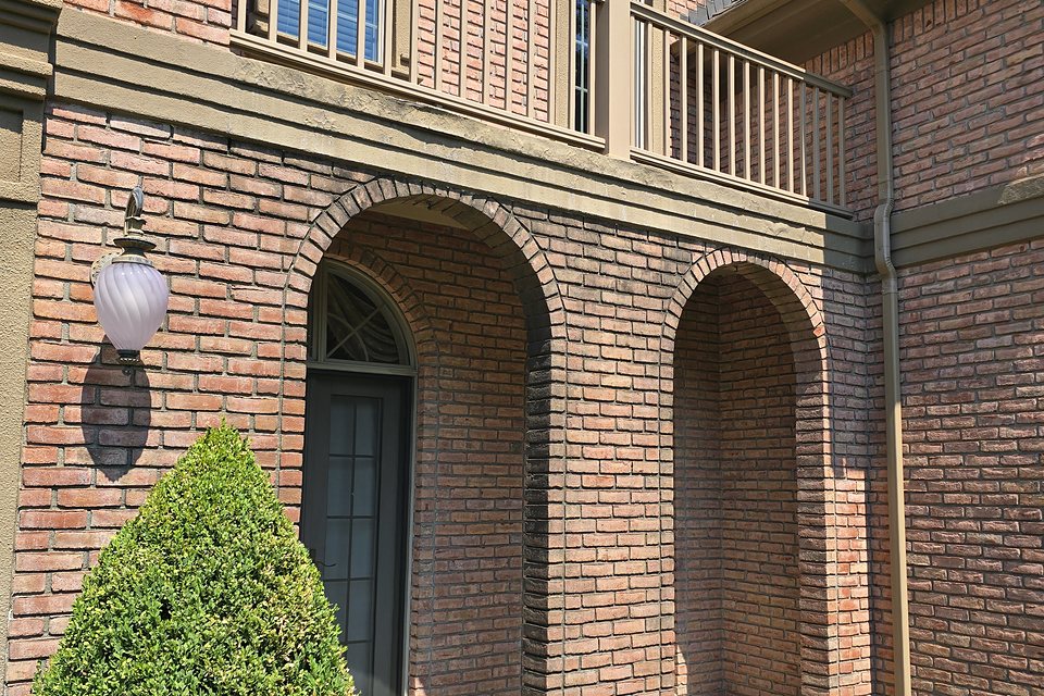 Before — weathered, cracked band under the balcony above the entry arches